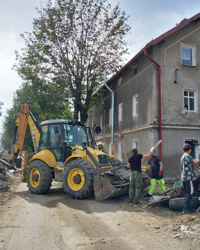 Koparko-ładowarka usuwa gruz z wąskiej ulicy obok kamienicy, kilku pracowników segreguje odpady — wywóz ziemi gruzu Ziemia Kłodzka, usługi koparko-ładowarką Kłodzko.